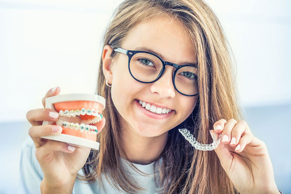 girl holding up braces and Invisalign aligners